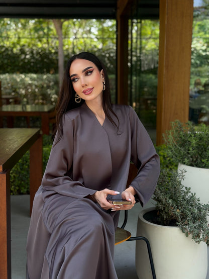 Woman in a gray dress sitting outdoors with greenery in the background